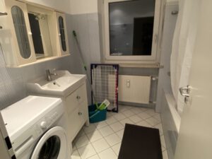 Ein voll ausgestattetes Badezimmer mit Dusche, Badewanne, Waschmaschine, Wäscheständer und Putzutensilien