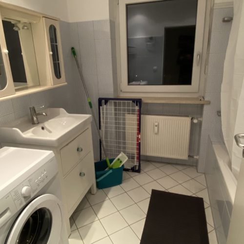 Ein voll ausgestattetes Badezimmer mit Dusche, Badewanne, Waschmaschine, Wäscheständer und Putzutensilien